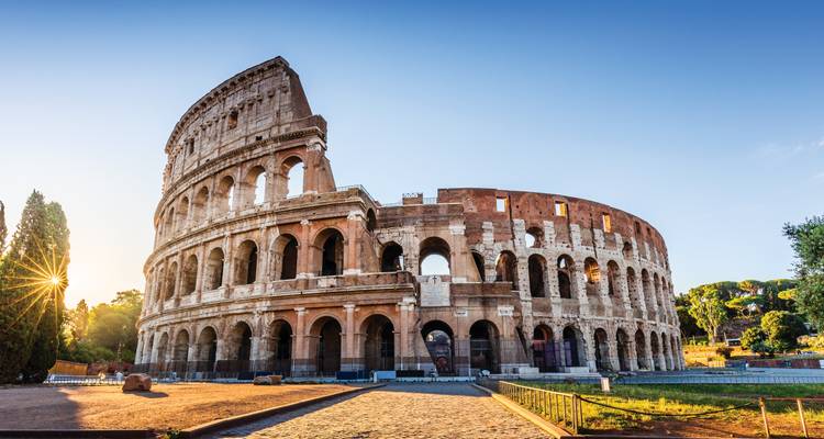 La lumière de l'aube illuminant le Colosseum antique à Rome avec un rayon de soleil traversant les arbres