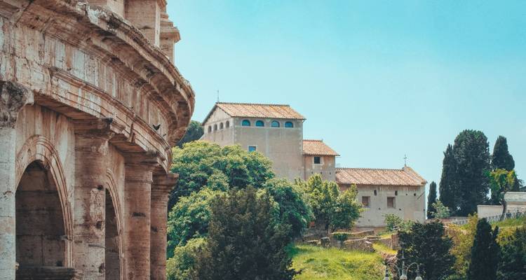 Vue latérale des arches du Colosseum avec des bâtiments rustiques et des cyprès à proximité