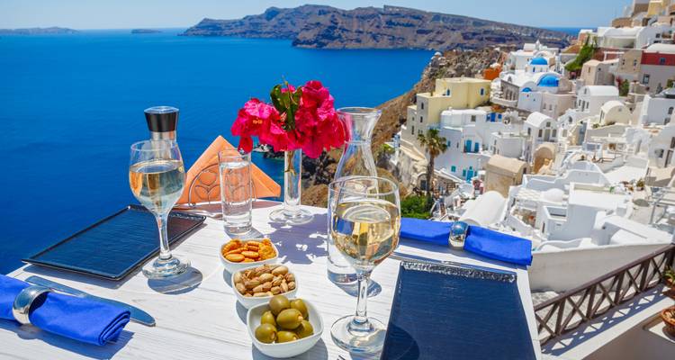 Table de restaurant en bord de mer avec vin et tapas offrant une vue sur la caldeira de Santorin et ses maisons blanches.