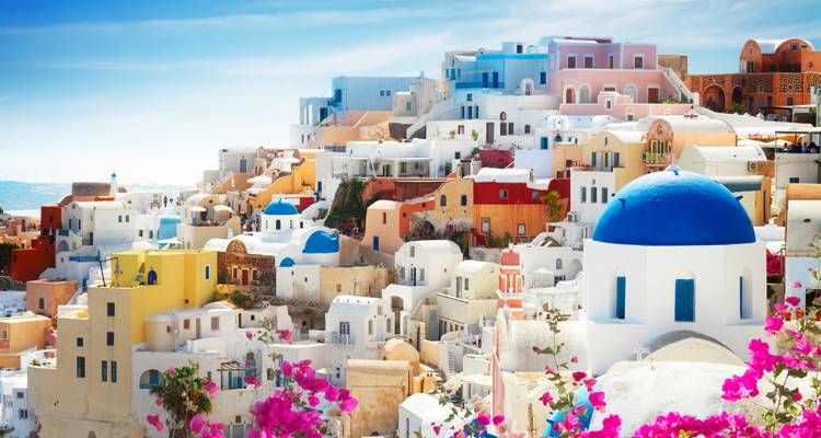 L'église emblématique aux dômes bleus et les maisons cubistes aux couleurs pastel de Santorin encadrées par les fleurs de bougainvillée.