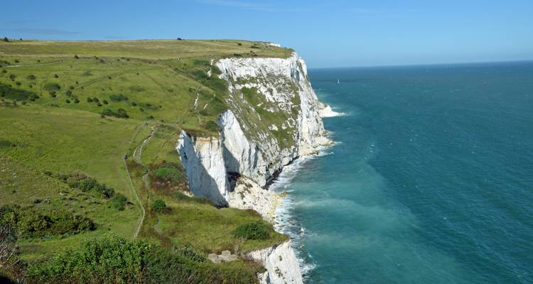 Des falaises de craie d'un blanc éclatant s'élevant au-dessus des eaux turquoise de la Manche avec un sentier sur les terres herbeuses du promontoire