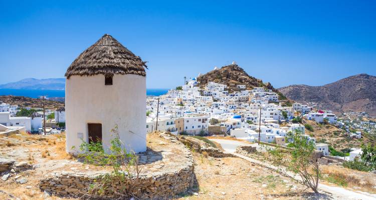 Traditional white windmill on a hill overlooking the whitewashed village of Chora on Ios island.