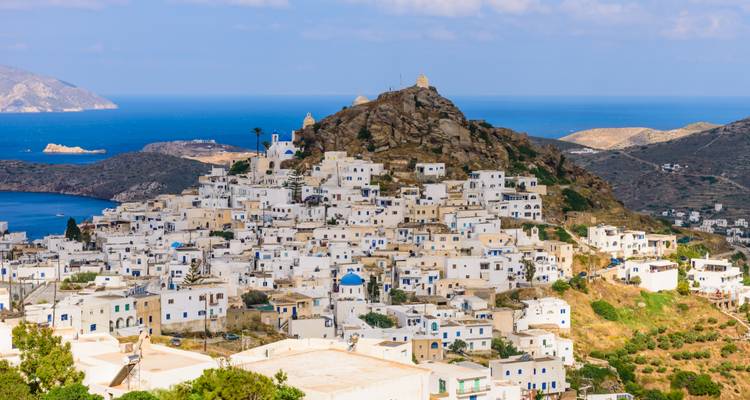 White cube houses of Ios climb a rocky hill above the deep blue Aegean Sea.