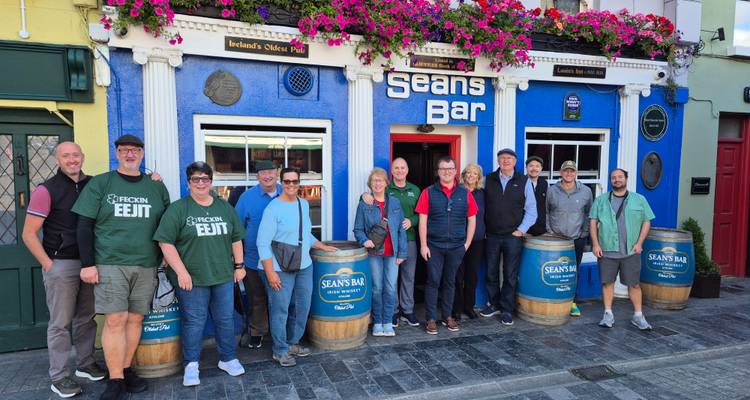 Groupe de touristes posant devant la façade colorée du Sean's Bar décorée de fleurs.