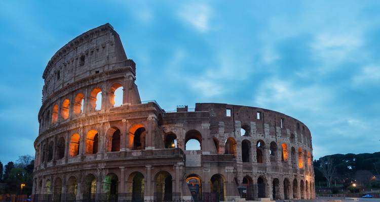 Het Colosseum verlicht met warm licht tegen een dramatische blauwe avondhemel in Rome