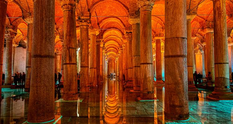 Intérieur ambiant d'une citerne souterraine avec des rangées infinies de colonnes anciennes illuminées se reflétant dans une eau immobile.