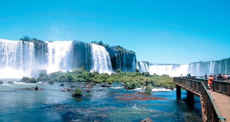 Visitantes en el paseo admirando las anchas cortinas de las Cataratas del Iguazú bajo un cielo despejado
