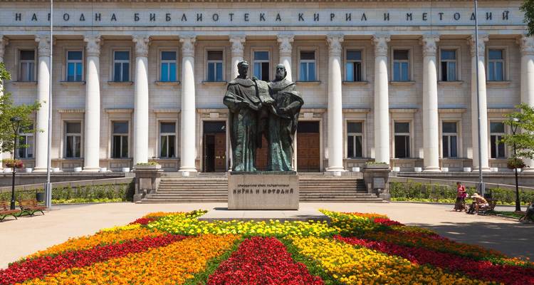 Statue of Cyril and Methodius with colorful flowerbeds in front of the National Library of Sofia.