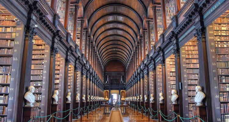 Grand vaulted hall of an old library lined with bookcases and marble busts