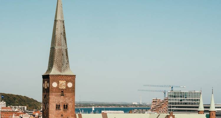 Hoog puntig kerktorentje dat uittorent boven een moderne kuststad