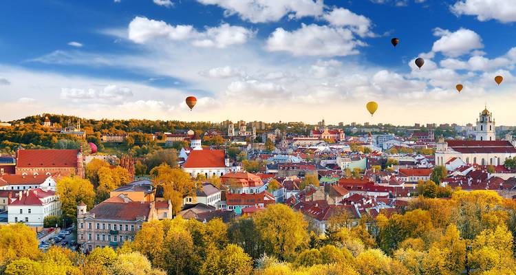 Autumnal city panorama dotted with hot air balloons over colorful foliage