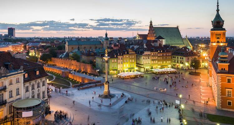 Evening aerial of Warsaw Old Town with warm lights and busy square below a pink sky