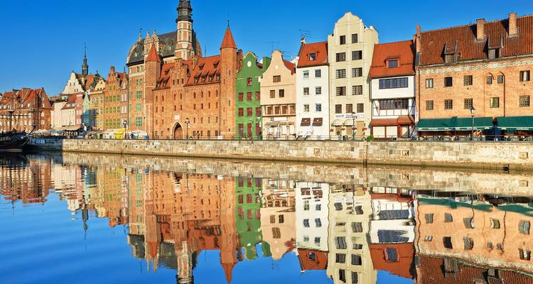Colorful Hanseatic merchant houses reflected perfectly in calm river under bright blue sky in Gdansk