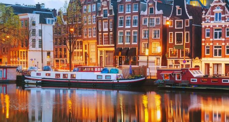 Les lumières du soir se reflétant sur un canal d'Amsterdam bordé de maisons historiques.