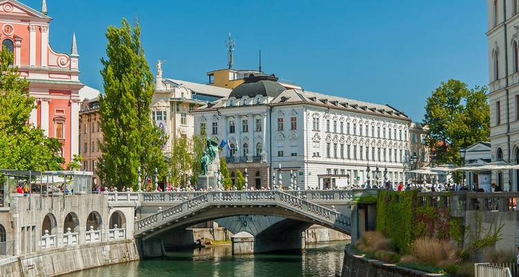 Drieduitse en pastelkleurige gebouwen over de rivier de Ljubljanica met wandelende voetgangers