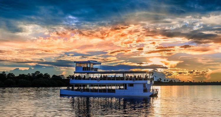 Crucero en barco de dos pisos por el río al atardecer con un cielo de colores dramáticos reflejándose en el agua tranquila.