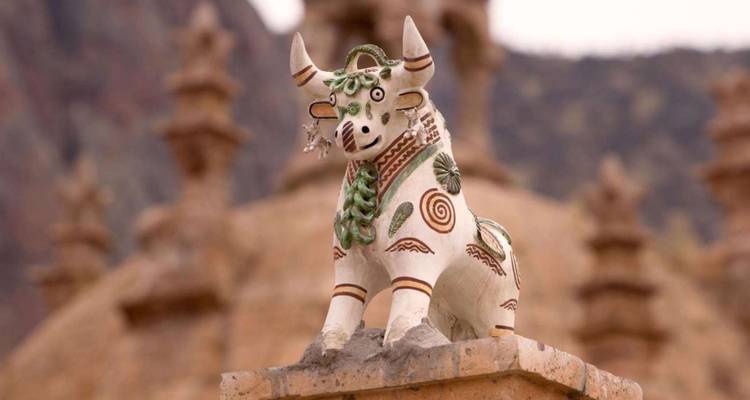 Decoratief keramisch Torito de Pucará stierbeeldje versierd met groene motieven tegen een wazig Andaans achtergrond.
