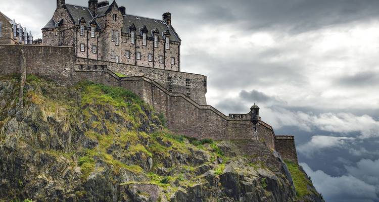 Stone Edinburgh Castle perched on a rocky crag beneath dramatic cloudy skies.