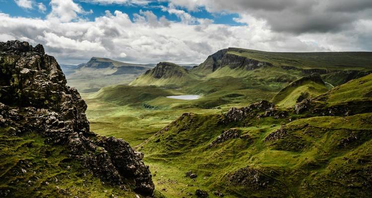 Dramatic green highland landscape with craggy ridges, loch and brooding clouds.