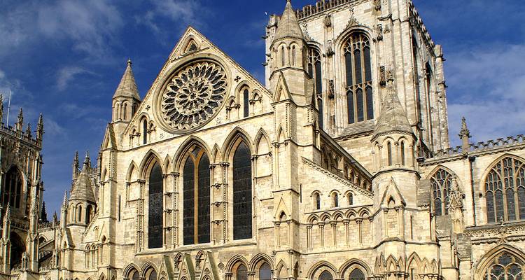 Detailed view of the ornate Gothic façade and large rose window of York Minster against a blue sky.
