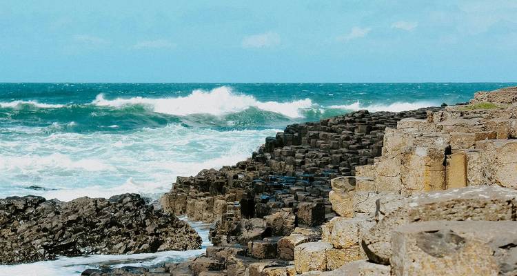 Basaltsäulen des Giant's Causeway treffen auf tosende Wellen unter klarem blauen Himmel