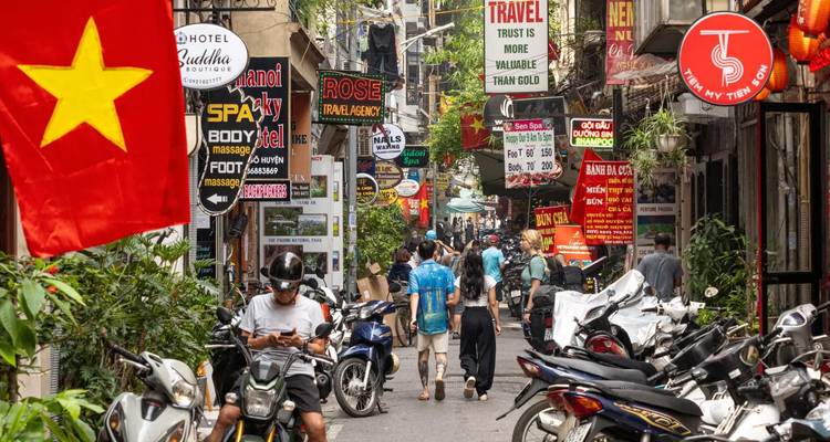 Busy narrow street in Hanoi’s Old Quarter lined with motorbikes, signboards and small shops.