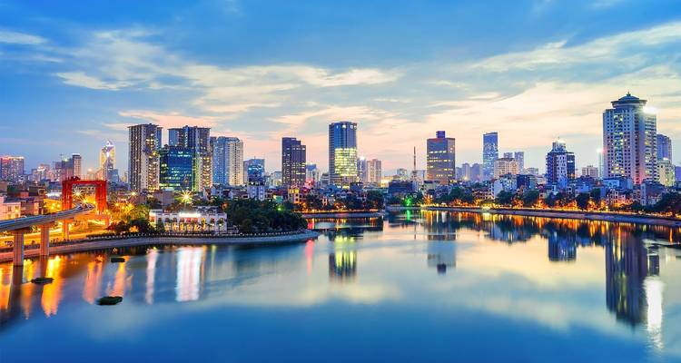 Evening skyline of Hanoi reflects on a calm river as city lights begin to glow.