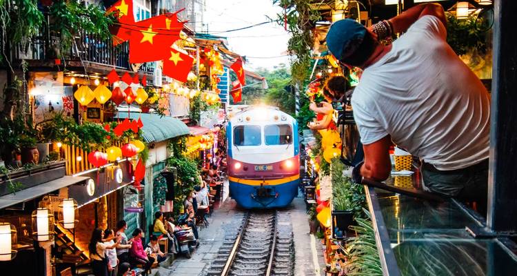 A train squeezes through lively Hanoi Train Street cafes as onlookers capture the moment.