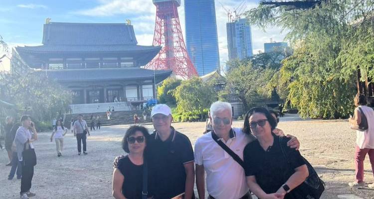 Travellers pose for a photo in a temple courtyard with Tokyo Tower rising behind them.