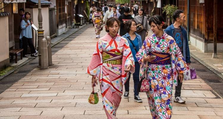 Two women wearing colorful kimonos stroll along a historic stone street lined with wooden houses.