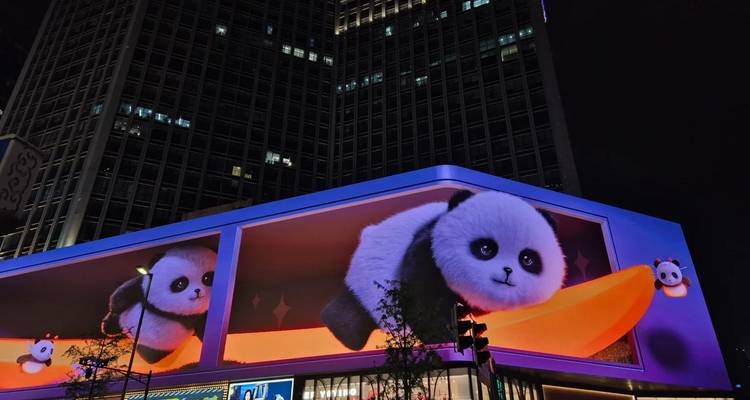 Nighttime 3D billboard displays animated pandas on a skyscraper façade illuminated with neon lights.