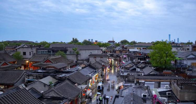 Evening view over Beijing hutong rooftops with narrow lanes lit by shop lights after rain.