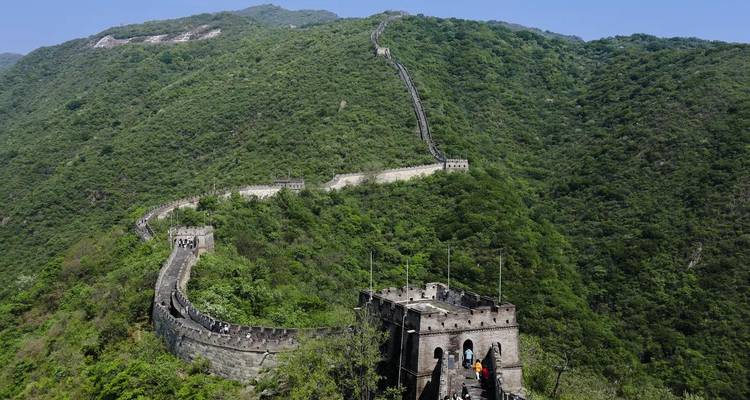 The Great Wall of China snakes along green mountain ridges under a clear blue sky.