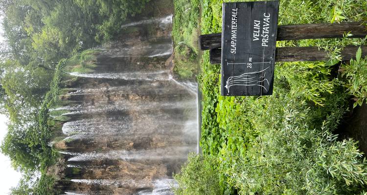 Tall cascade of Veliki Prštavac waterfall behind a wooden signpost showing its height