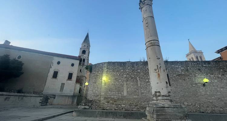 Ancient stone column and surrounding ruins at dusk with blue twilight sky in Zadar