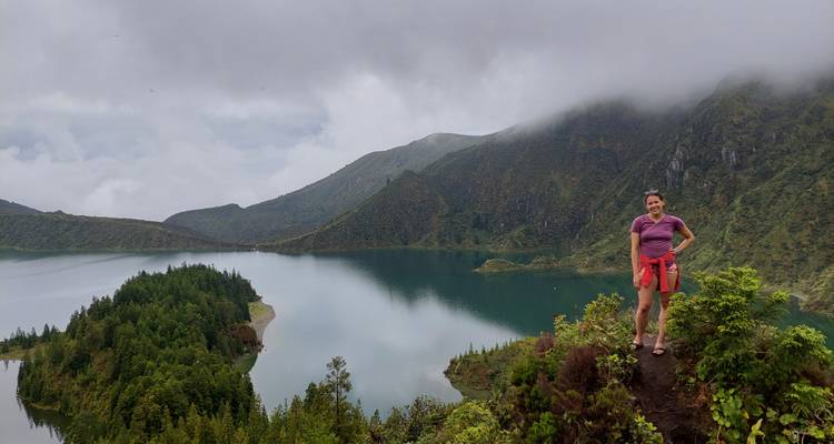 Le voyageur se tient au bord d'une falaise avec une vue panoramique du lac de cratère enveloppé de brouillard en contrebas.