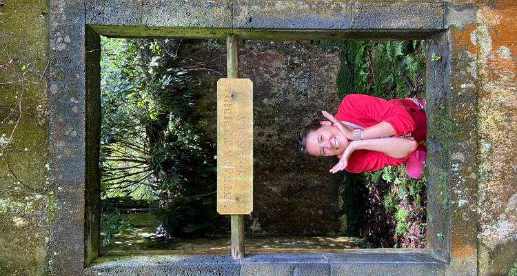 Femme joyeuse encadrée par une ouverture de fenêtre couverte de mousse d'une ruine en pierre dans la forêt.
