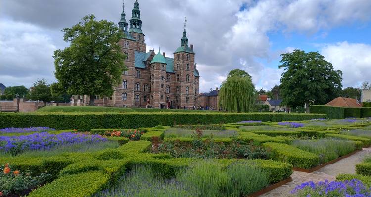 Le château de Rosenborg de style Renaissance s'élevant au-delà de jardins de fleurs formels et de haies bien entretenues sous un ciel partiellement nuageux et lumineux.