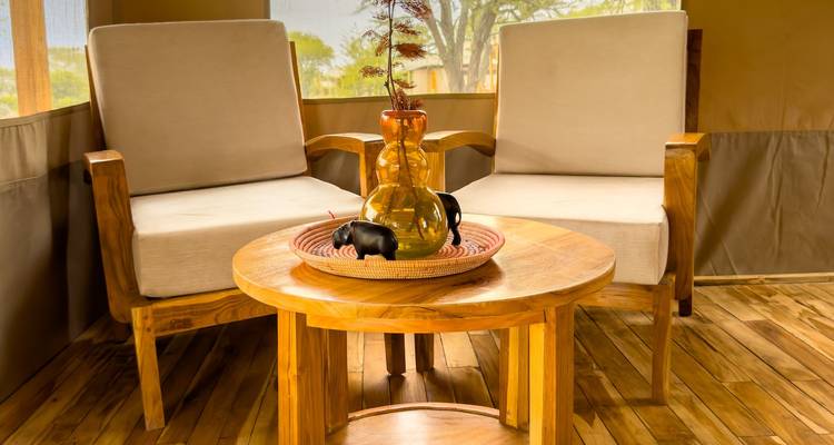 Cozy safari-style lounge with two armchairs and a small wooden table inside a canvas tent.