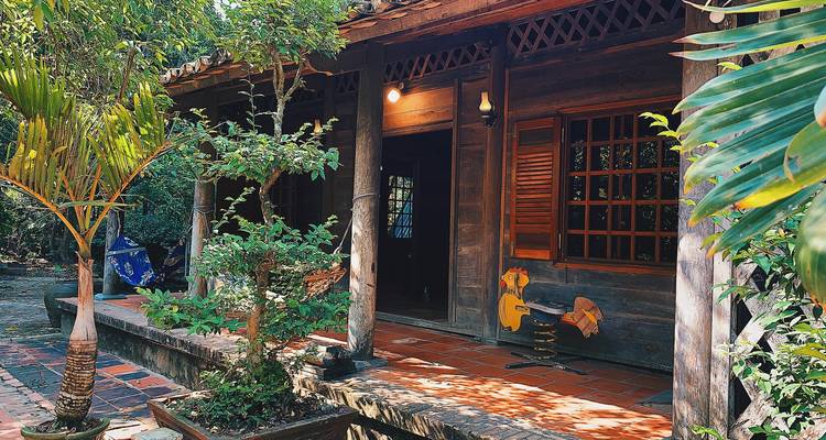 Homestay tradicional de madera en el Delta del Mekong con veranda de azulejos rodeada de plantas exuberantes.