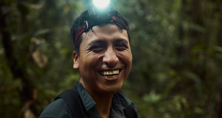 Close-up of a smiling guide wearing a headlamp in the dim Amazon rainforest.