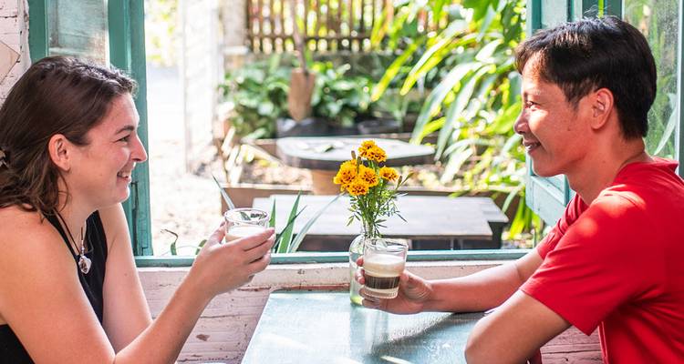Un homme et une femme savourent un café glacé à la fenêtre d'un café lumineux et verdoyant.
