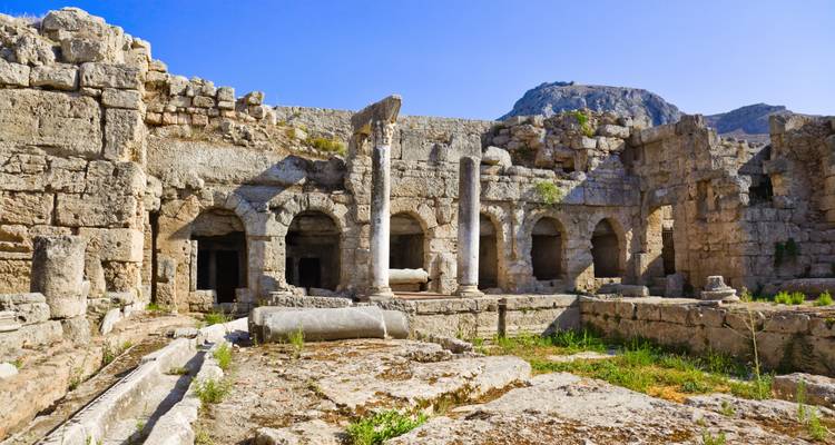 Interior view of ancient stone ruins and arches in Corinth beneath a clear blue sky.