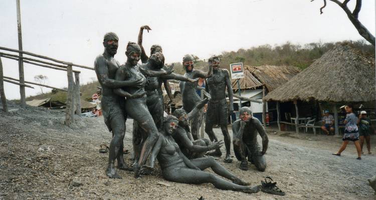 Travelers covered head to toe in volcanic mud posing playfully near rustic huts