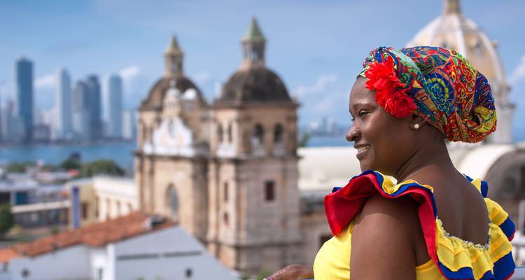 Traditional palenquera woman smiling with historic domes and modern Cartagena skyline behind