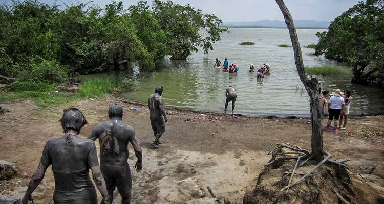 Group of tourists covered in grey volcanic mud walking toward a lake for rinsing off