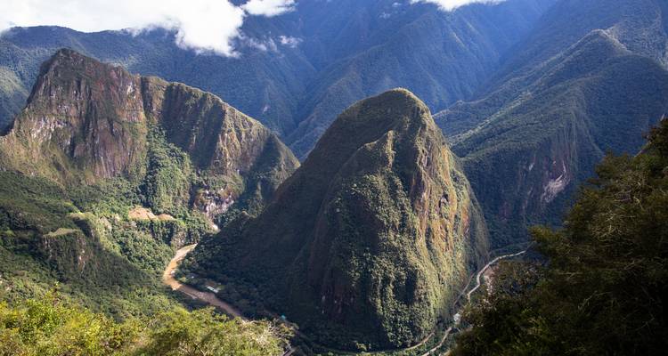 Sheer green mountains and a winding river frame the dramatic peak of Huayna Picchu under clear skies.