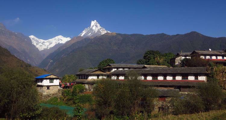 Village ensoleillé de la vallée de montagne avec le pic acéré du Machhapuchhare s'élevant derrière.