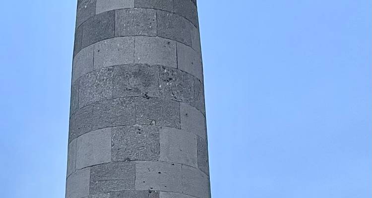 Tall grey stone column rising into a clear blue sky