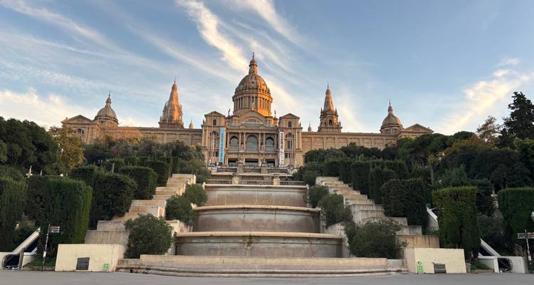 Grande façade du Museu Nacional d'Art de Catalunya surplombant des fontaines étagées et des haies soigneusement entretenues.